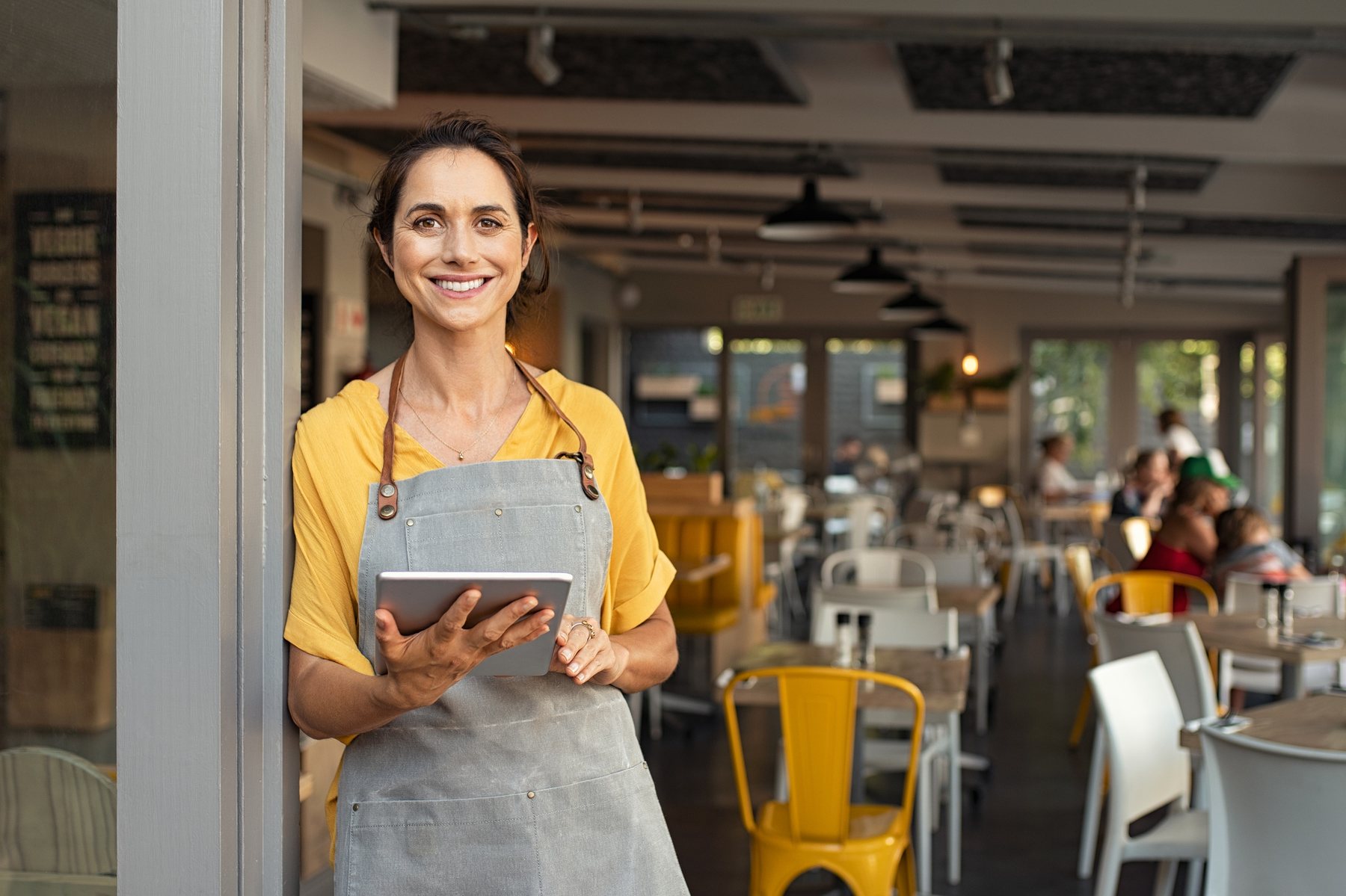 A business owner standing in the doorway of her café, holding a tablet